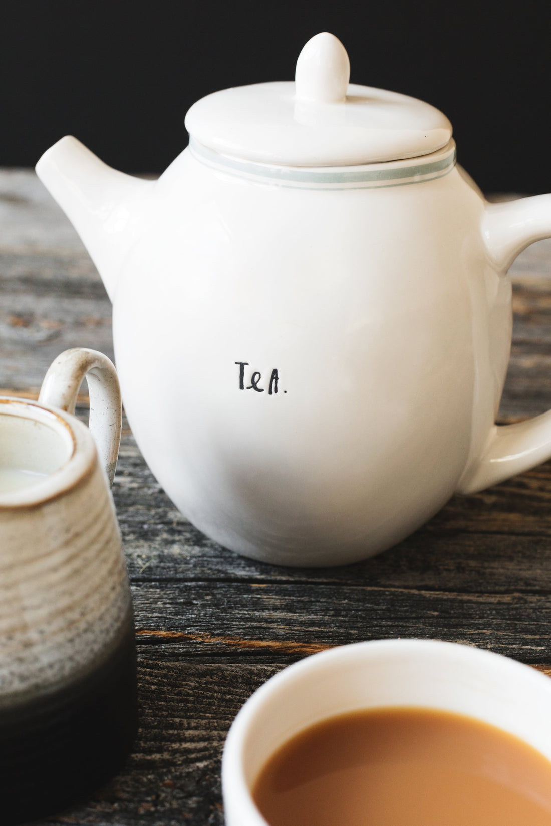 White teapot and teacup resting on a wooden table.